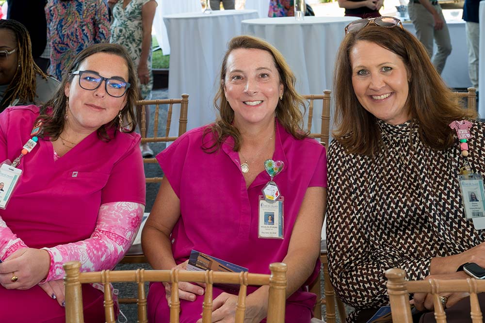 Two women wearing bright pink scrubs and a third woman wearing a dark shirt. All three are smiling.